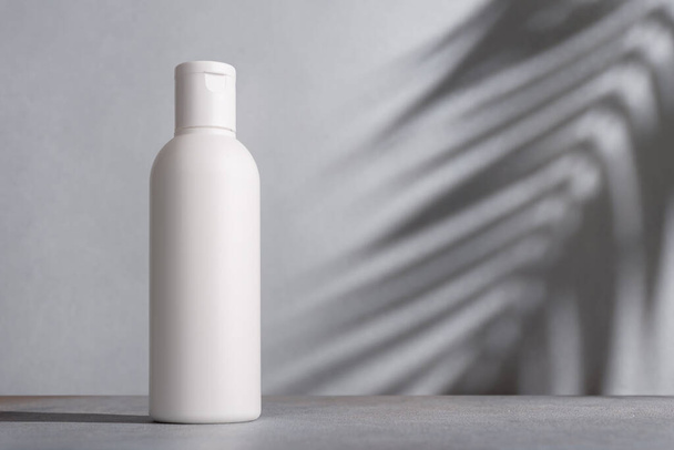 White blank packaging cosmetic plastic bottle with shadow of palm leaves. Spa and grooming product.  - Foto, afbeelding