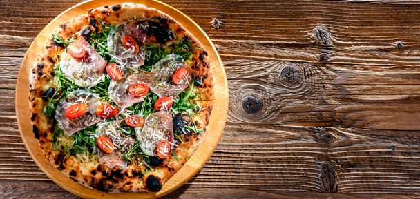 Pizza Italiana podawana z szynką, serem, pomidorami i rukolą. - Zdjęcie, obraz