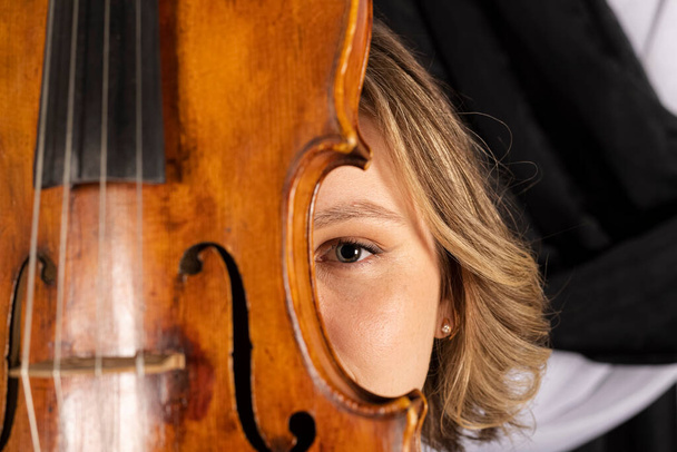 Junge elegante Mädchen posieren mit einer Geige. Porträt einer Geigerin vor einem schwarz-weißen Vorhang. - Foto, Bild
