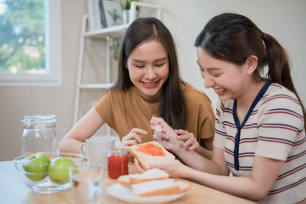glückliche asiatische Frauen frühstücken in der Tischküche. zwei schöne Frauen essen morgens Essen. - Foto, Bild