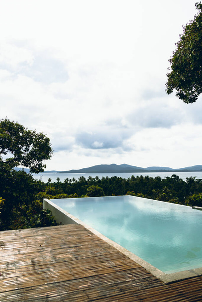 Wide angle view of a beautiful infinity pool in a tropical island overlooking the sea and other islands of exotic archipelago. Overcast day, almost sunset, water reflections. - Фото, изображение