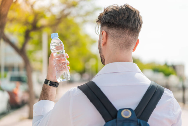 Νεαρός όμορφος άντρας με ένα μπουκάλι νερό στην πίσω θέση - Φωτογραφία, εικόνα