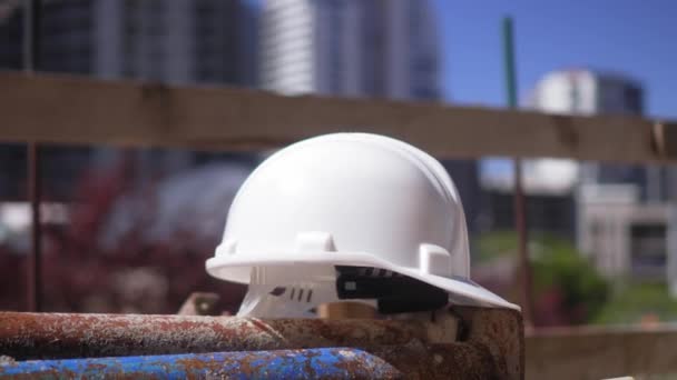 White construction helmet rests on metal reinforcement as symbol of construction and engineering. Construction site on sunny day against backdrop of fence and blue sky. - Footage, Video