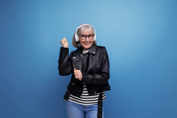 ενεργητικός κομψό σύγχρονο μεσήλικας γυναίκα με γκρίζα μαλλιά ακούει μουσική σε ακουστικά σε ένα φωτεινό φόντο με αντίγραφο χώρο. - Φωτογραφία, εικόνα