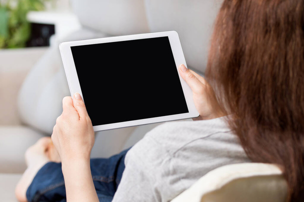 Back view of a woman watching media content showing a blank laptop screen sitting on a sofa at home - Foto, Imagem