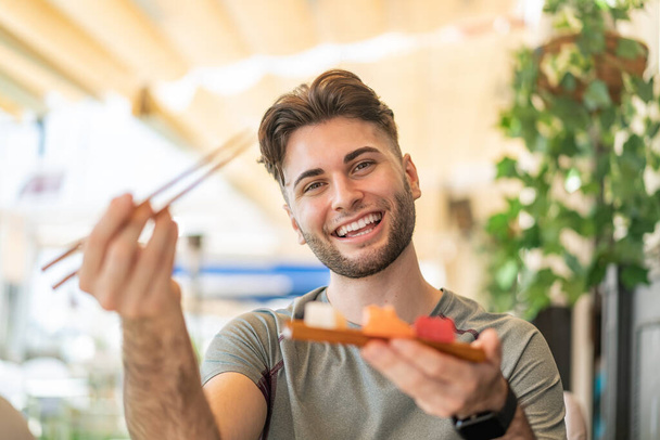 Young handsome man holding sashimi at outdoors - 写真・画像