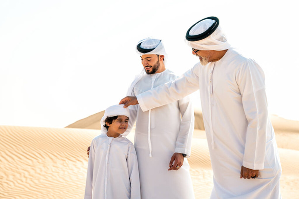 Three generation family making a safari in the desert of Dubai wearing white kandura outfit. Grandfather, son and grandson spending time together in the nature. - Zdjęcie, obraz