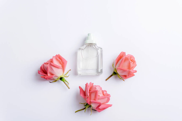 Glass perfume bottle and coral pink rose flowers on white background. Top view, flat lay, mockup. - Photo, Image