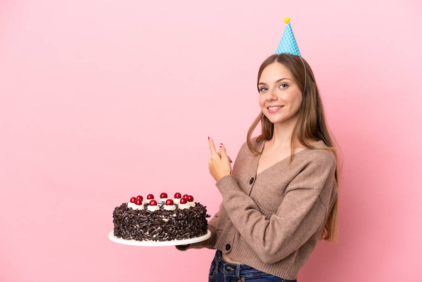 Giovane donna lituana in possesso di torta di compleanno isolato su sfondo rosa puntando indietro - Foto, immagini