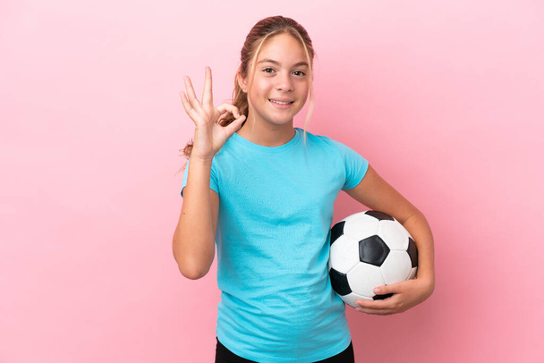 Маленькая девочка футболист изолирован на розовом фоне показывая ОК знак с пальцами - Фото, изображение