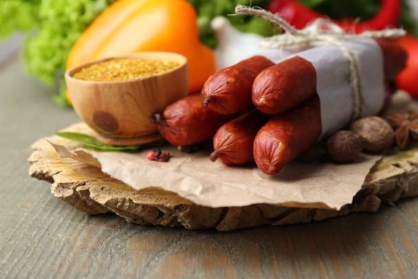 Composition of smoked thin sausages, mustard in bowl and spices on cutting board, on wooden background - Φωτογραφία, εικόνα