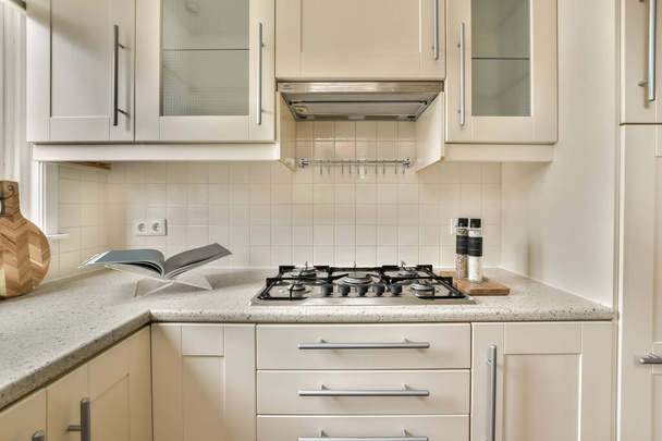 kuchnia z białymi szafkami i sprzętem na blacie przed kuchenką, która służy do gotowania - Zdjęcie, obraz