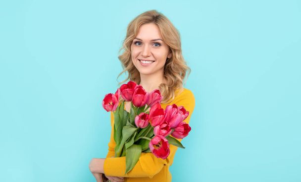 blij jonge vrouw met lente tulp bloemen op blauwe achtergrond. - Foto, afbeelding