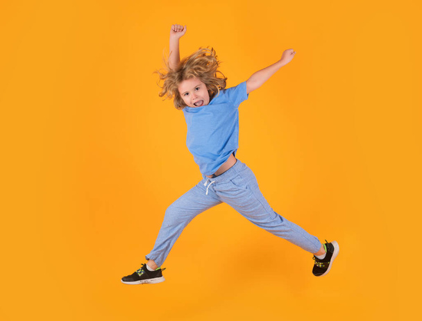 Kid jongen springen vliegen beweging dragen shirt en jeans geïsoleerd op gele studio achtergrond - Foto, afbeelding