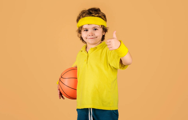 Little basketballer with basketball ball showing thumb up. Child in sportswear with basketball. Sport game. Active sport lifestyle. Basketball training. Smiling kid basketball player with game ball - Fotoğraf, Görsel