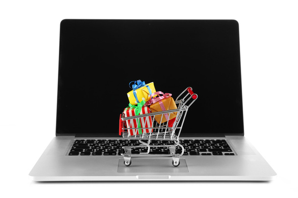 Laptop com carrinho de compras pequeno cheio de presentes isolados no fundo branco
 - Foto, Imagem