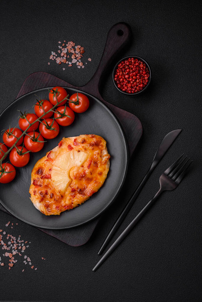 Grilled chicken fillet in the form of a steak with tomatoes, pineapple and cheese on a dark concrete background - Foto, Bild