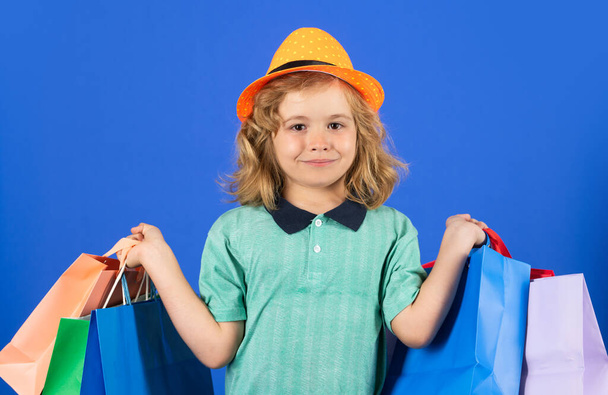 Модный ребенок на шоппинге. Портрет ребенка с сумками. Счастливчик держит сумки с покупками. Студийный портрет. Концепция продажи и скидки - Фото, изображение