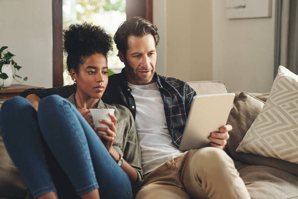 Love, home and couple with a tablet, connection and social media for communication, romance and relax. Partners, man and woman on a couch, interracial and technology for chatting, texting and bonding. - Foto, Imagen