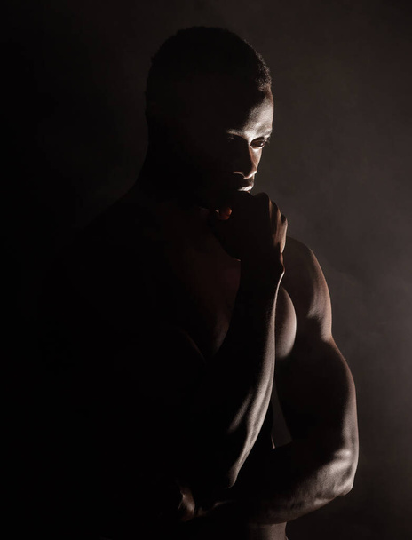 Black man, muscle silhouette and studio for thinking, anxiety and depression with art deco vision. Model, art aesthetic and depressed with strong body, alone or suffering with mental health in shadow. - Photo, Image