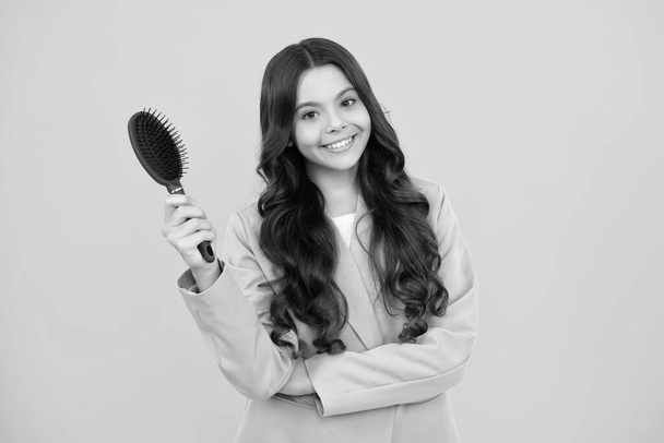 Teenager brushing combing hair with big comb on yellow isolated studio background. Teen girl with hairbrush. Kids hairstyle. Happy positive and smiling emotions of teenager girl - Foto, Imagem