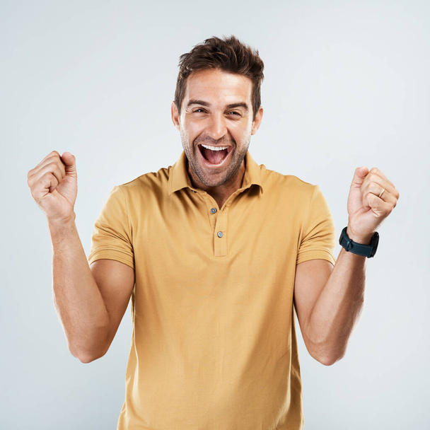 I agree with you all the way. Portrait of a cheerful young man punching the air in excitement while standing against a grey background - Фото, изображение