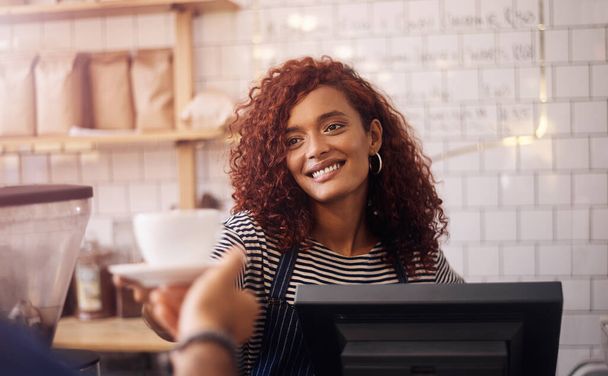 Happy woman, barista and cup of coffee to customer in cafeteria, restaurant shop and food service industry. Waitress, worker and giving drinks order, cappuccino and tea with smile in small business. - Photo, Image