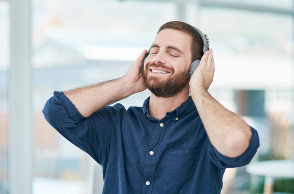 Ha jól érzed magad, jól csinálod. egy boldog fiatal üzletember fejhallgatóval egy modern irodában - Fotó, kép