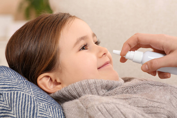 Mother using nasal spray to treat her little daughter on sofa, closeup - Foto, Imagen