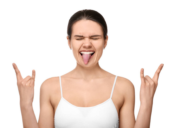 Happy young woman showing her tongue and rock gesture on white background - Foto, Bild