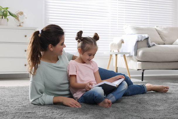 Young mother and her daughter reading book on floor at home - Foto, imagen
