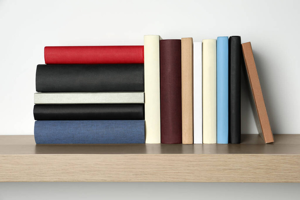 Many hardcover books on wooden shelf near white wall - Фото, изображение
