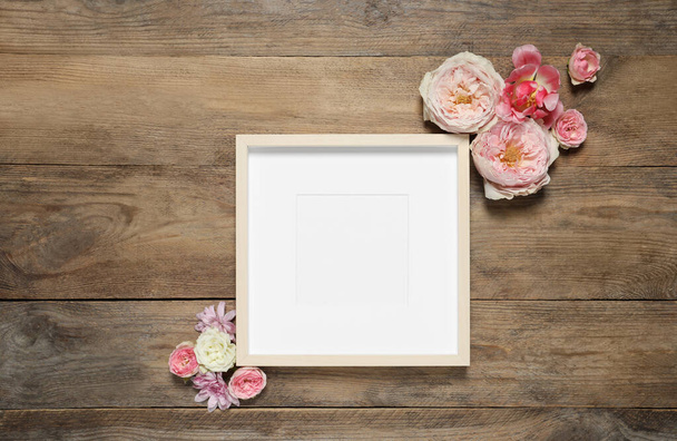Empty photo frame and beautiful flowers on wooden table, flat lay. Space for design - Fotografie, Obrázek