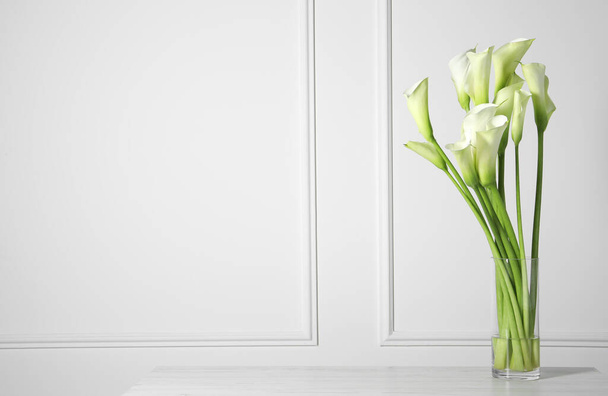 Beautiful calla lily flowers in vase on white table. Space for text - Foto, Imagem