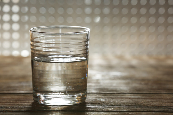 Glass of clean mineral water on wooden surface and lattice background - Foto, Bild