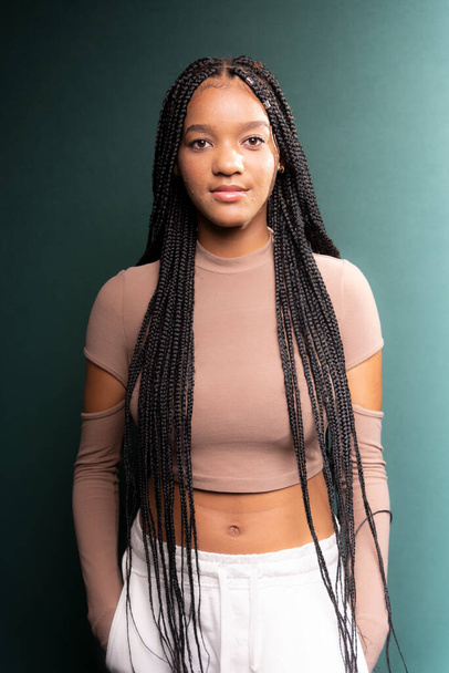 Portrait of beautiful young woman, standing, with big braids in her hair. Isolated on dark green background - Foto, Imagen