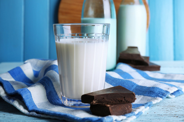 Vidro e garrafas de leite com pedaços de chocolate em guardanapo despojado e fundo tábuas de madeira cor
 - Foto, Imagem