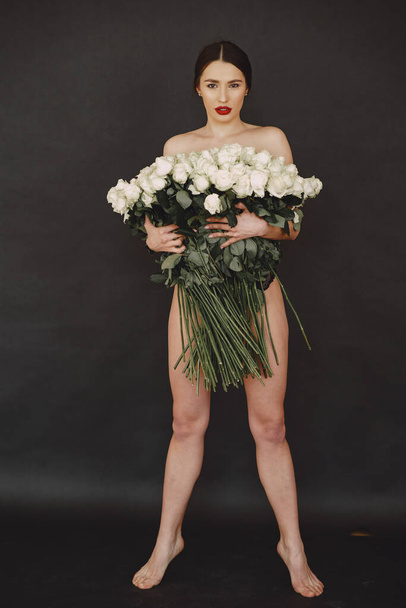 Beautiful girl in a studio. Stylish girl on a black background. Lady with bouquete of roses. - Foto, imagen
