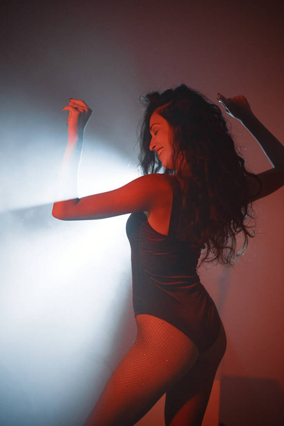 Young curly brunette girl posing for a photo. Girl wearing red velour bodysuit. Projectors light girl up. - 写真・画像