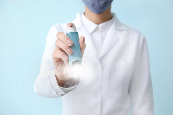 Médico femenino con inhalador sobre fondo azul claro, primer plano - Foto, Imagen