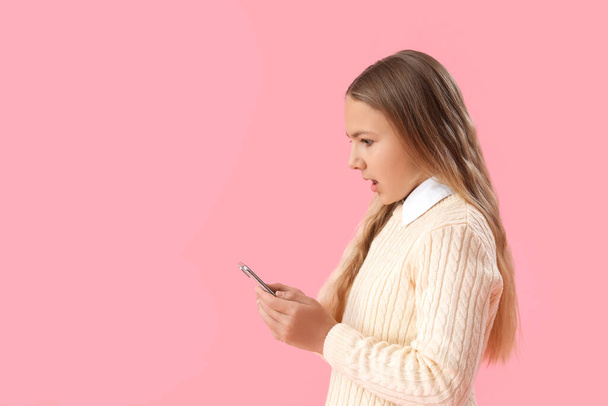 Shocked little girl using mobile phone on pink background - Фото, зображення