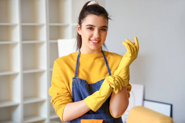 jonge vrouw het aantrekken van rubber handschoenen voor het schoonmaken van haar huis - Foto, afbeelding