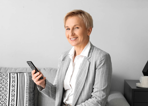 Mulher de negócios madura com telefone celular sentado no sofá no escritório - Foto, Imagem
