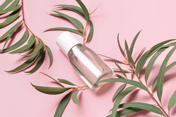 Bottle of micellar water with plant branches on pink background, closeup - Foto, Bild