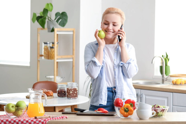 Elmalı genç bir kadın mutfakta cep telefonuyla konuşuyor. - Fotoğraf, Görsel
