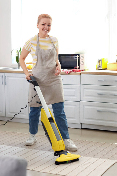 Young woman hoovering carpet in kitchen - 写真・画像