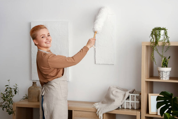 Jeune femme nettoyage peinture avec pp-duster à la maison - Photo, image
