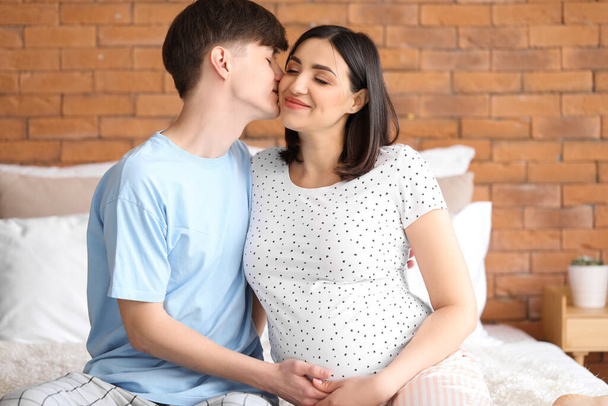 Νεαρό έγκυο ζευγάρι κάθεται στο υπνοδωμάτιο - Φωτογραφία, εικόνα