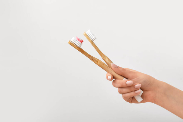 Female hand with bamboo toothbrushes and paste on grey background - Foto, Imagem