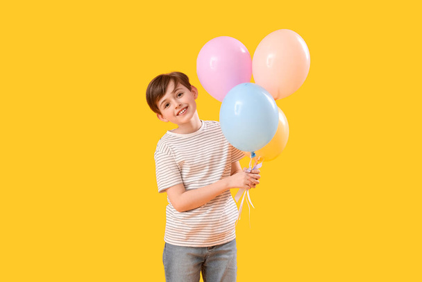 Kleine jongen met ballonnen op gele achtergrond. Kinderfeestviering - Foto, afbeelding